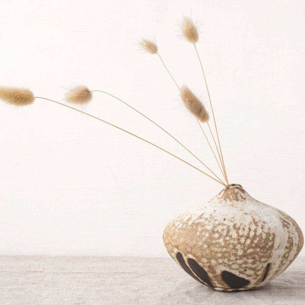 Ceramic vase with dried grass on a neutral surface in soft natural light.